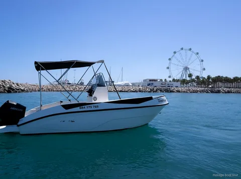 Lancha blanca con toldo cerca del rompeolas del puerto y una noria en un paseo en barco por Málaga