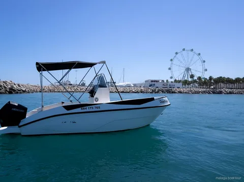 Witte motorboot met zonnetent bij de havendam en een reuzenrad tijdens een boottocht Malaga