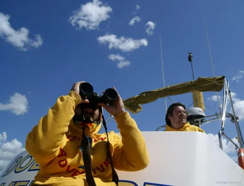 Crewmitglied im gelben Pullover mit Fernglas unter blauem Himmel bei einer Bootstour Malaga
