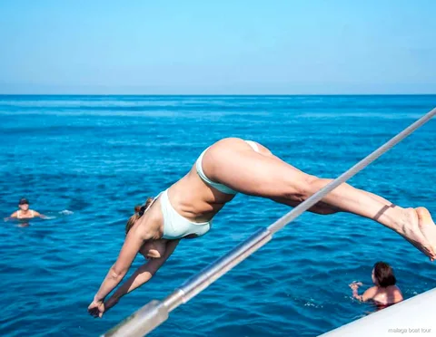 Mulher a mergulhar do catamarã para a água azul num passeio de barco em Málaga