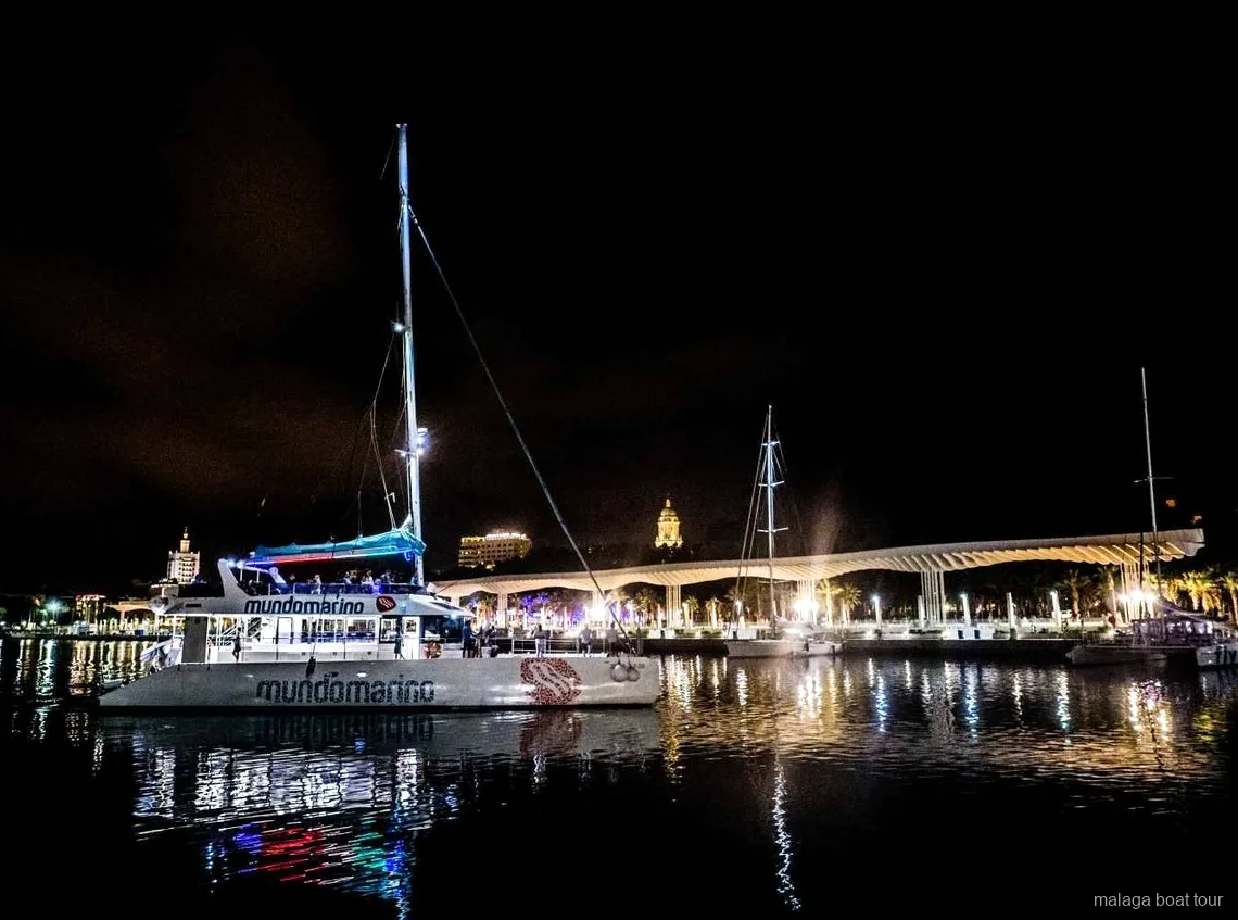 Catamarã atracado à noite junto ao passeio iluminado do porto num passeio de barco em Málaga