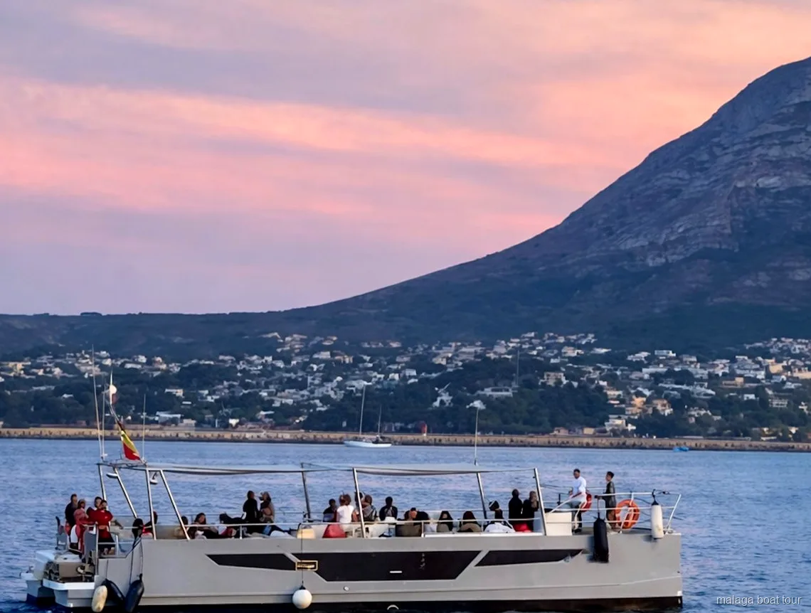 Catamarã com passageiros no convés ao entardecer sob um céu rosa num passeio de barco em Málaga