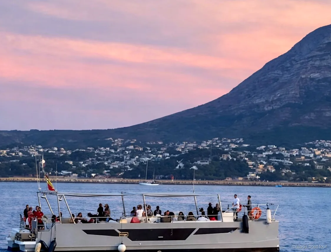 Catamarán con pasajeros en cubierta al anochecer bajo un cielo rosado en un paseo en barco por Málaga