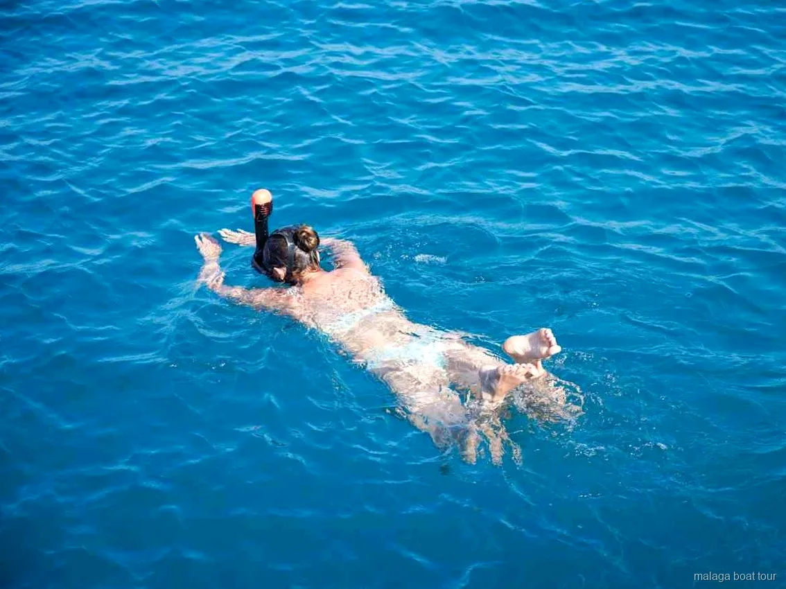 Persona con máscara de snorkel flotando en agua azul y clara en un paseo en barco por Málaga