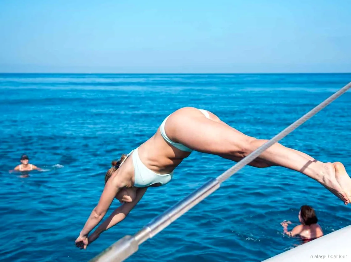 Mujer en pleno salto desde la barandilla del catamarán al mar en un paseo en barco por Málaga