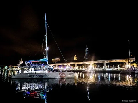 Catamaran amarré de nuit près de la promenade illuminée du port lors d'une balade en bateau à Malaga