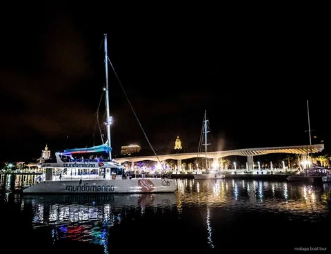 Catamarán amarrado de noche junto al paseo iluminado del puerto en un paseo en barco por Málaga