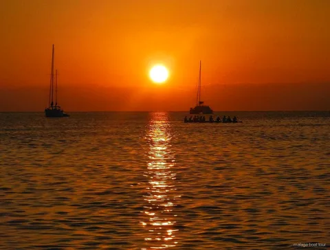 Coucher de soleil orange sur la mer, deux voiliers et un catamaran en silhouette, excursion en bateau à Malaga