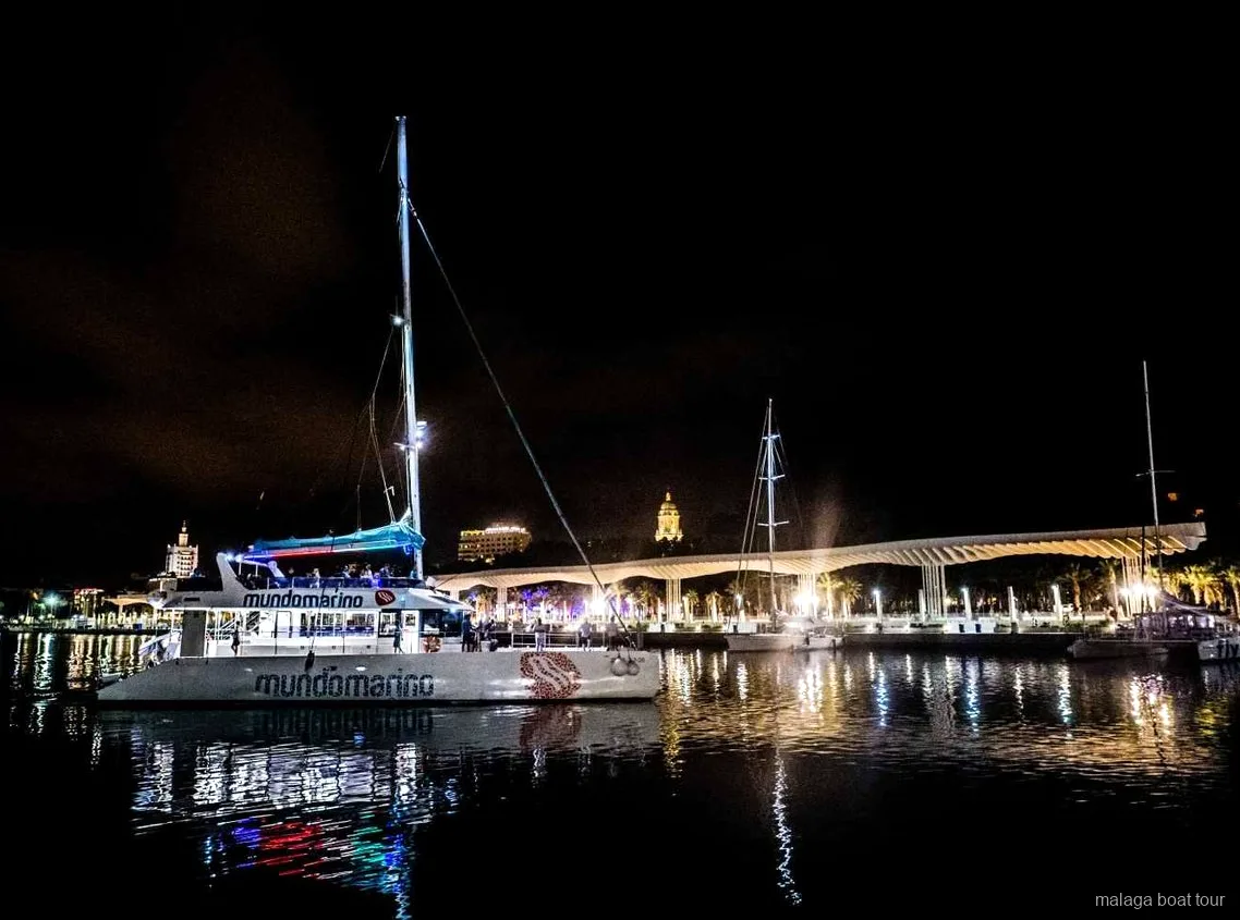 Catamaran 's nachts afgemeerd naast de verlichte havenpromenade tijdens een boottocht in Malaga