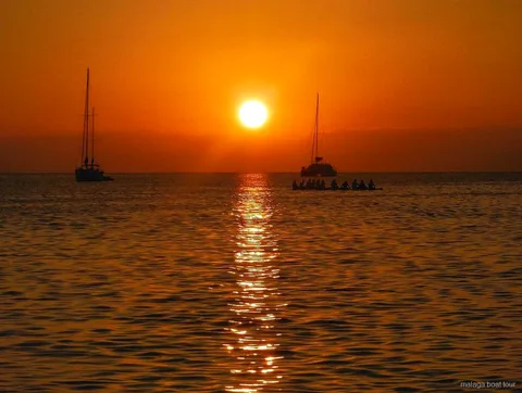 Oranje zonsondergang boven zee met twee zeilboten en een catamaran in silhouet tijdens een boottocht Malaga