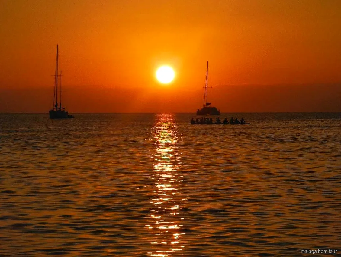Oranje zonsondergang boven zee met twee zeilboten en een catamaran in silhouet tijdens een boottocht Malaga
