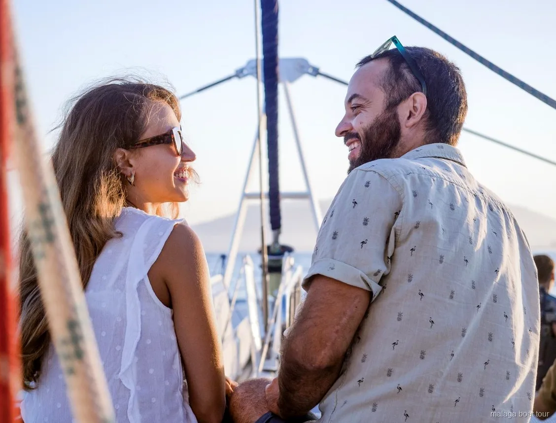 Lachend stel op het dek van een catamaran in warm avondlicht tijdens een boottocht Malaga
