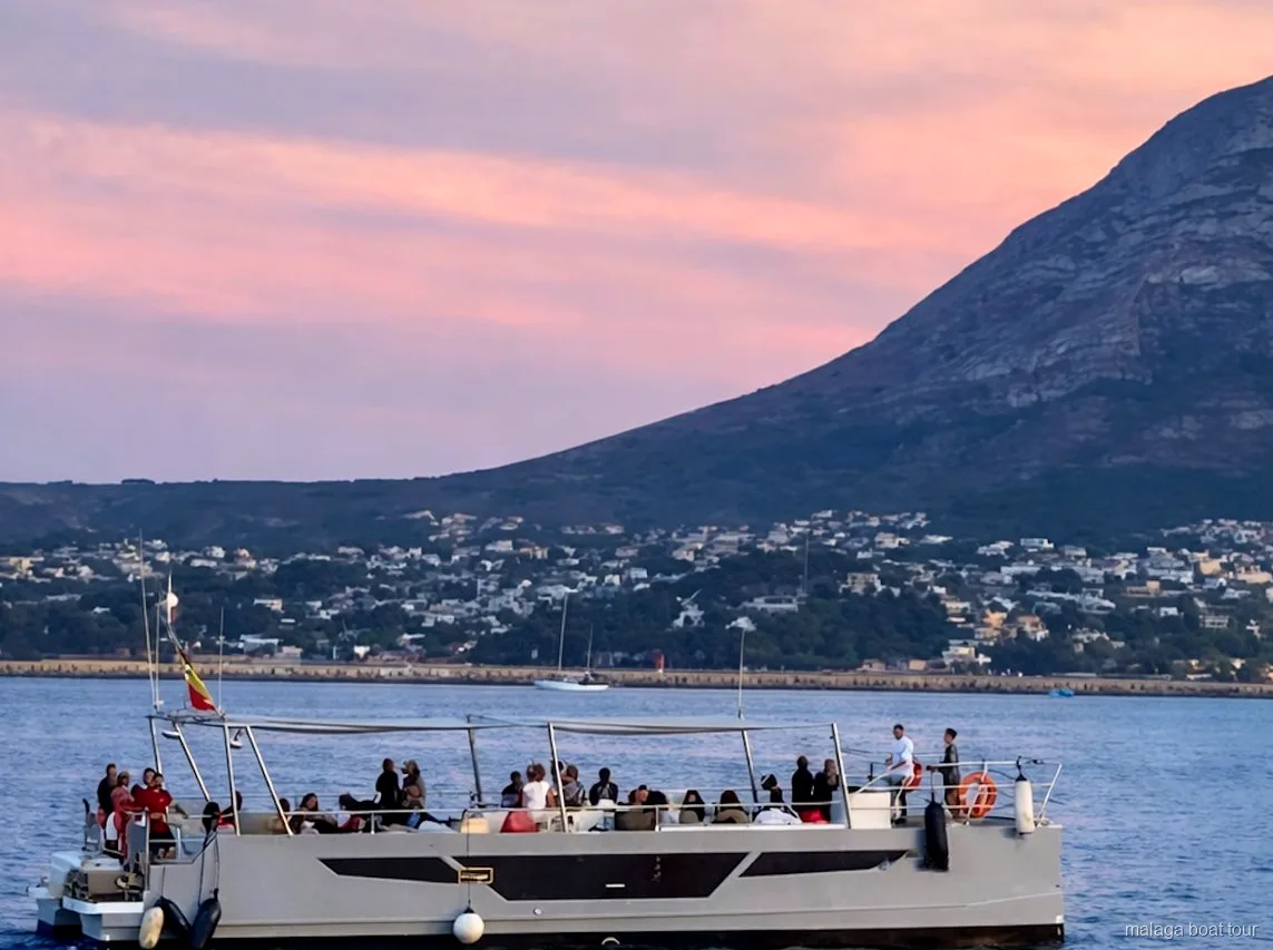Catamarano con passeggeri sul ponte al crepuscolo sotto un cielo rosa in una gita in barca a Malaga