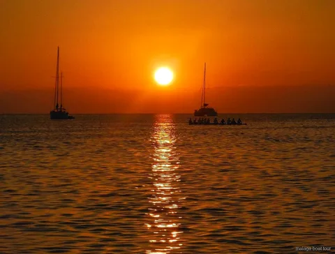 Tramonto arancione sul mare con due barche a vela e un catamarano in silhouette durante una gita in barca a Malaga