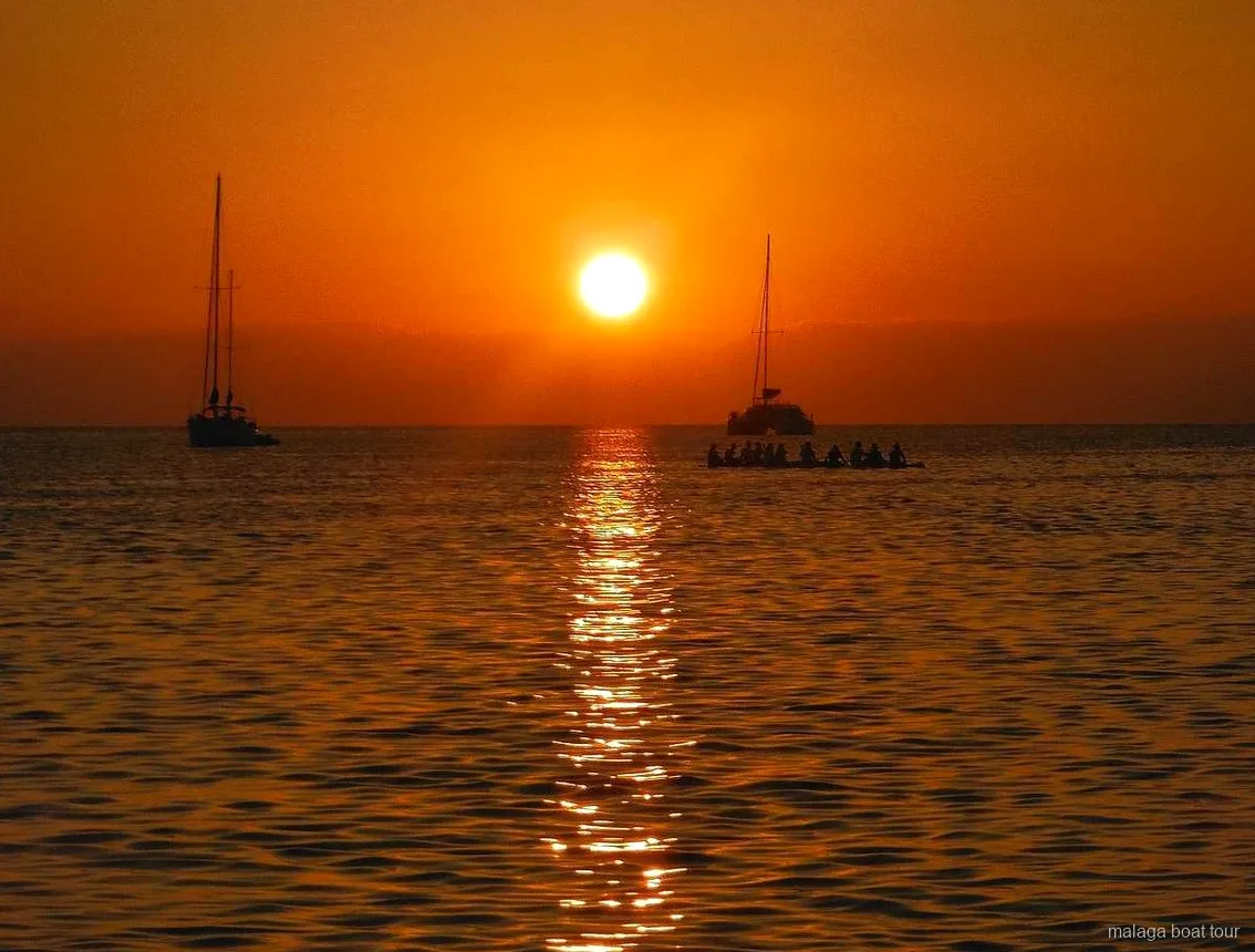 Tramonto arancione sul mare con due barche a vela e un catamarano in silhouette durante una gita in barca a Malaga