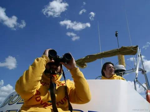 Membre d'équipage en sweat jaune qui scrute avec des jumelles sous un ciel bleu, excursion en bateau à Malaga