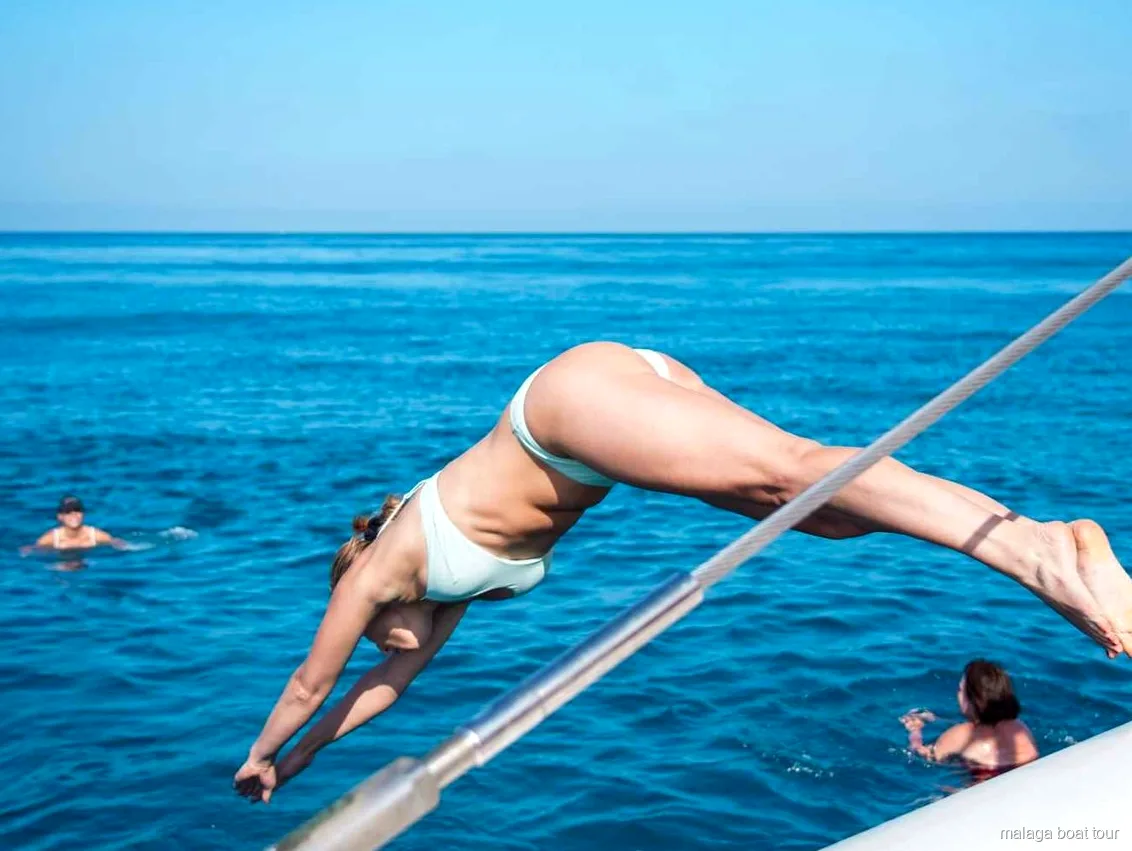 Frau mitten im Kopfsprung von der Reling des Katamarans ins Meer bei einer Bootstour in Malaga