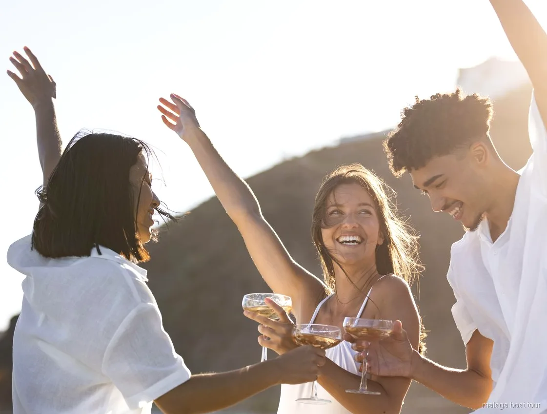 Friends dancing and toasting with glasses in warm evening light on a Malaga boat tour