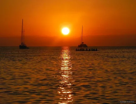 Orange solnedgång över havet med två segelbåtar och en katamaran i siluett under en båttur i Malaga