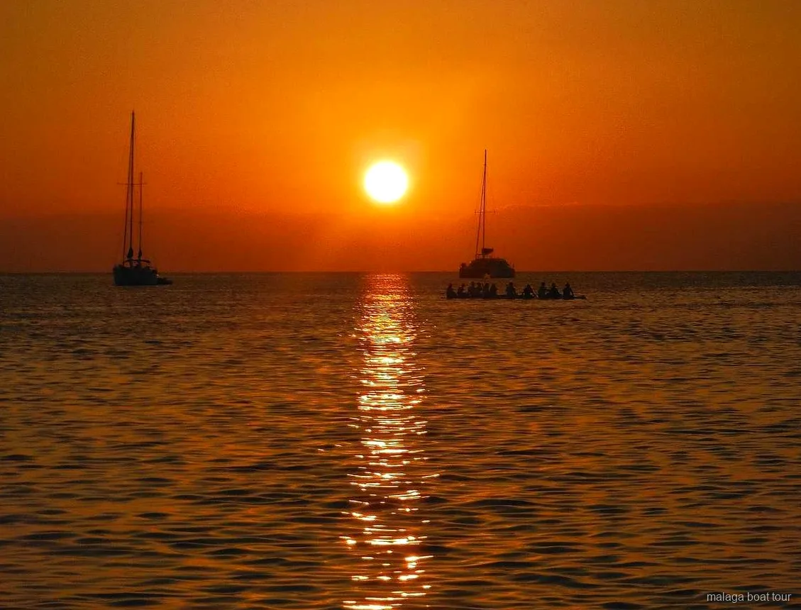 Orange solnedgång över havet med två segelbåtar och en katamaran i siluett under en båttur i Malaga