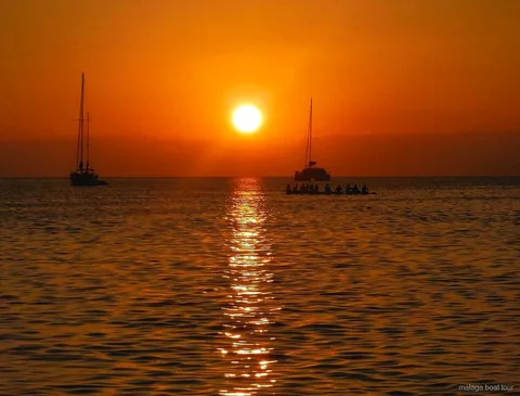 Orangefarbener Sonnenuntergang über dem Meer mit zwei Segelbooten und einem Katamaran bei einer Bootstour Malaga