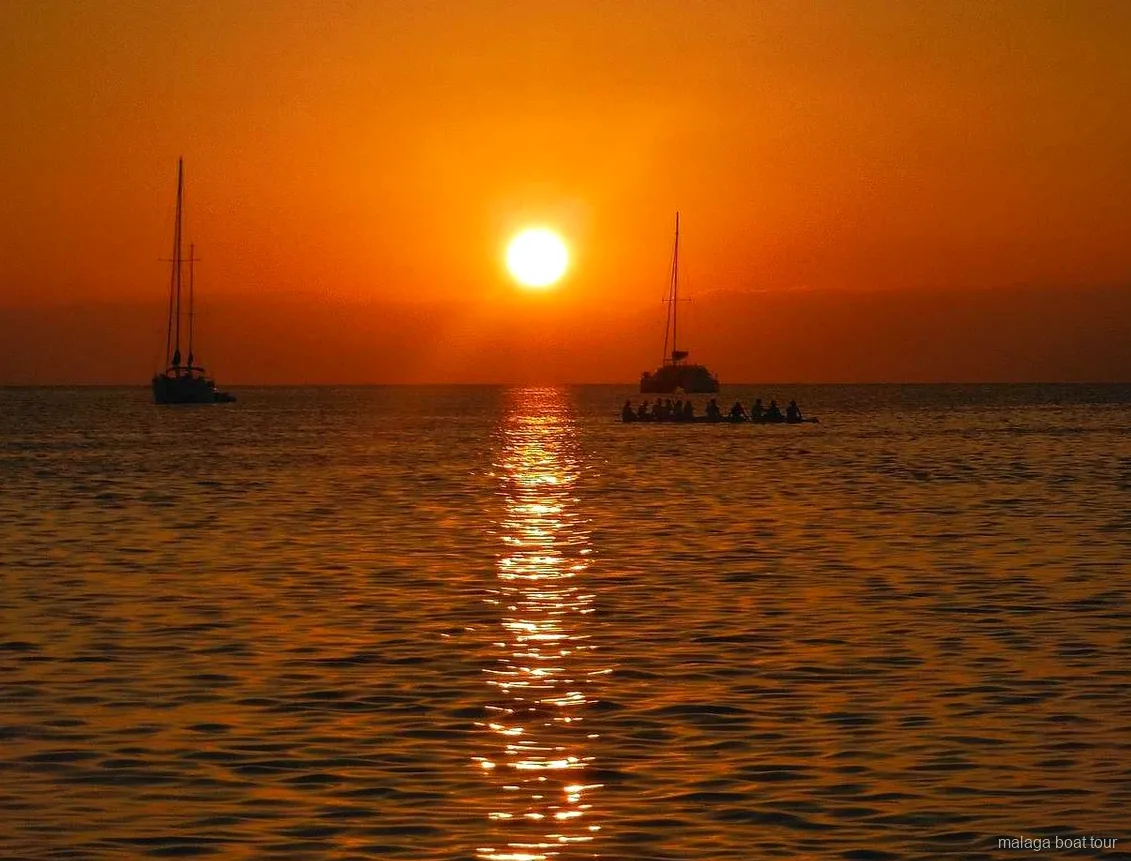 Orangefarbener Sonnenuntergang über dem Meer mit zwei Segelbooten und einem Katamaran bei einer Bootstour Malaga