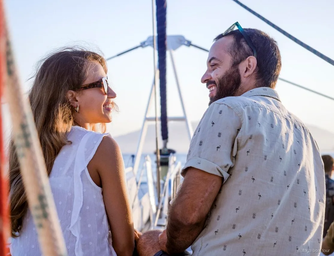 Lächelndes Paar auf dem Deck eines Katamarans im warmen Abendlicht bei einer Bootstour Malaga
