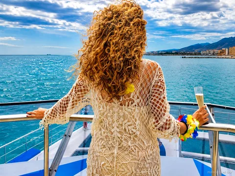 Woman in a crochet dress holding a glass on a catamaran deck facing the coast on a Malaga boat tour