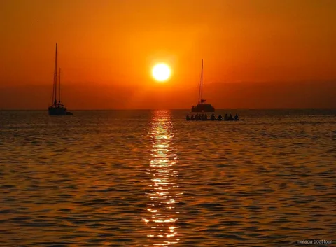 Orange sunset over the sea with two sailboats and a catamaran in silhouette on a Malaga boat tour