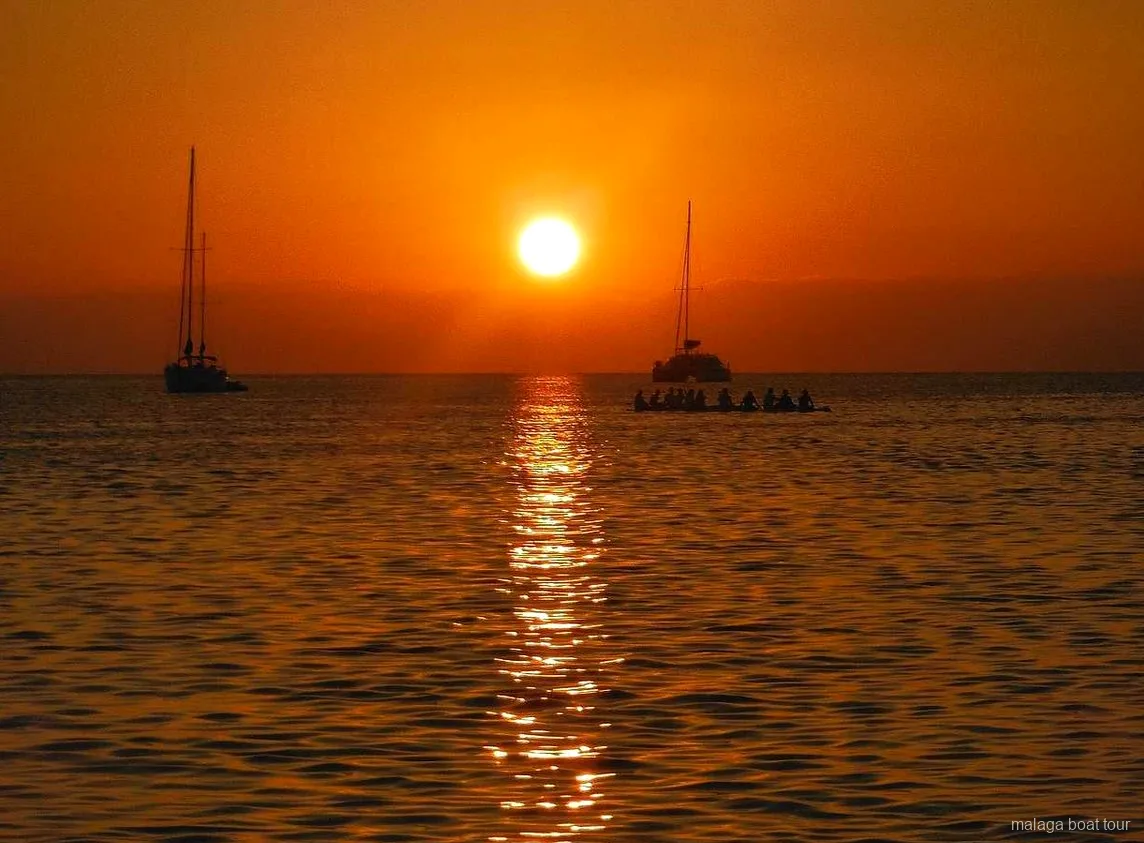 Orange sunset over the sea with two sailboats and a catamaran in silhouette on a Malaga boat tour