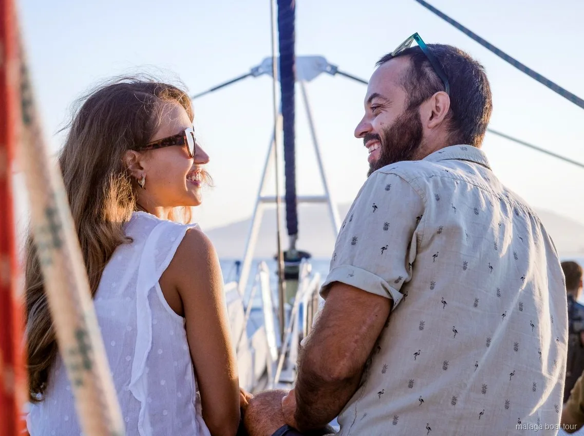 Smiling couple on the deck of a catamaran in warm evening light during a Malaga boat tour